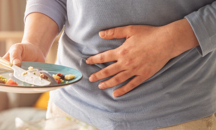 Man holding his stomach in pain while carrying an empty dinner plate of scraps
