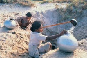 Young girls collecting water from holes dug in the ground, Udaipur, India.