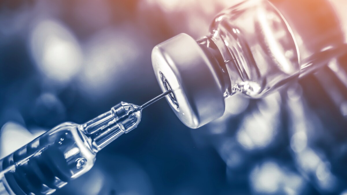 A syringe removes liquid from a bottle, representing SARS-CoV-2 vaccine development