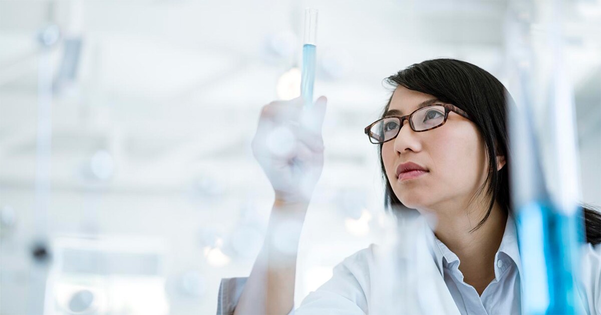 A researcher gazes at a test tube filled with light blue liquid, symbolizing vaccine development for RNA viruses