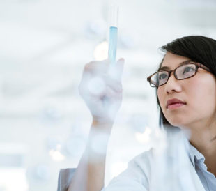 A researcher gazes at a test tube filled with light blue liquid, symbolizing vaccine development for RNA viruses