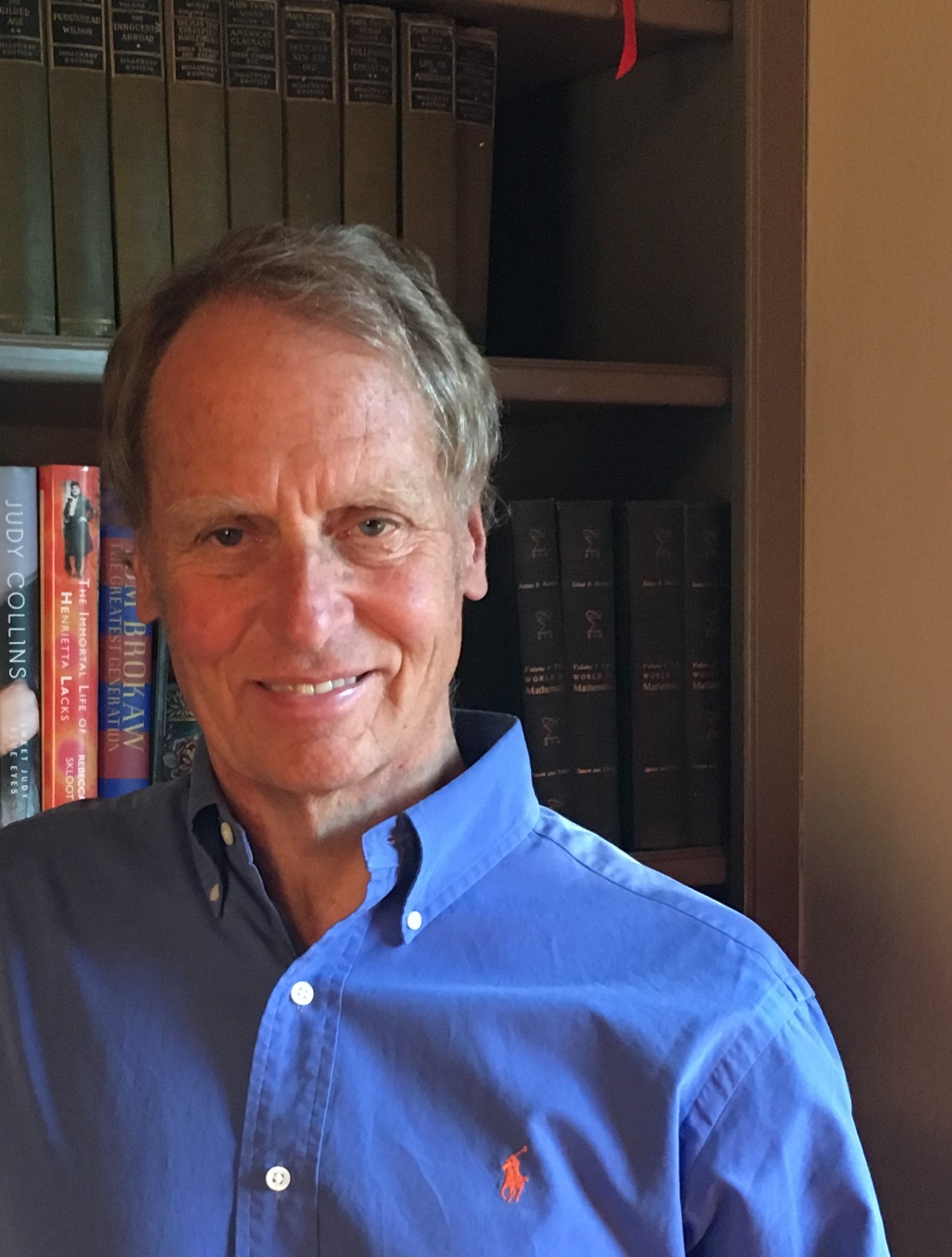 John Carlquist smiles while standing in front of his bookshelf