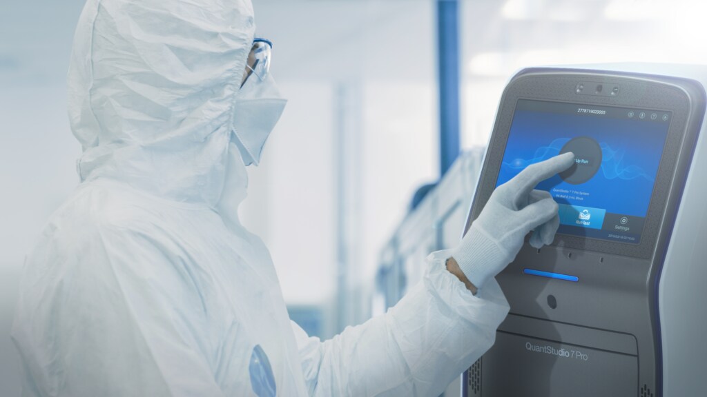 Scientist in clean room suit and mask using QuantStudio instrument.