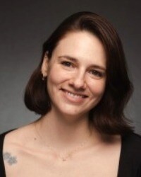Headshot of a woman smiling with shoulder-length brown hair against a neutral background.
