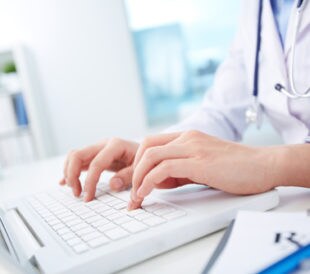 Close-up of hands of a nurse typing on laptop. Image: Kaspars Grinvalds/Shutterstock.com.