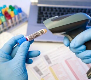 Technician hands scanning bar codes on biological sample tube in the lab of blood bank. Image: angellodeco/Shutterstock.com.