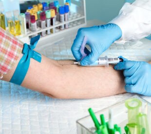 Laboratory with nurse taking a blood sample from patient, in background samples blood and urine tubes. Image: angellodeco/Shutterstock.com.