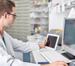 Male scientist in biotech lab working on a computer and tablet using eProcurement Manager software.