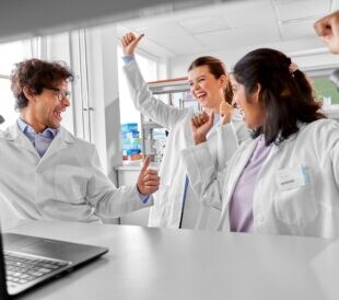Male and two female scientist celebrating in a biotech laboratory
