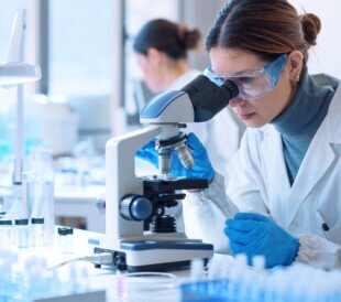 Young scientists conducting research investigations in a medical laboratory, a researcher in the foreground is using a microscope