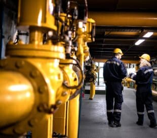 Engineers walking by gas pipelines inside refinery production plant.