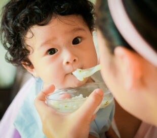 Curly-haired asian baby being fed with a spoon