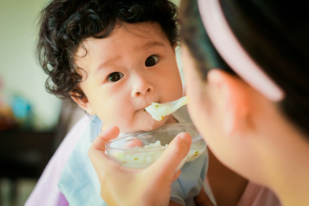 Curly-haired asian baby being fed with a spoon