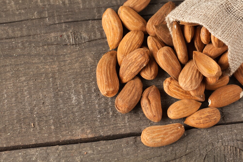 Raw almonds spilling out of a burlap bag onto a wooden background