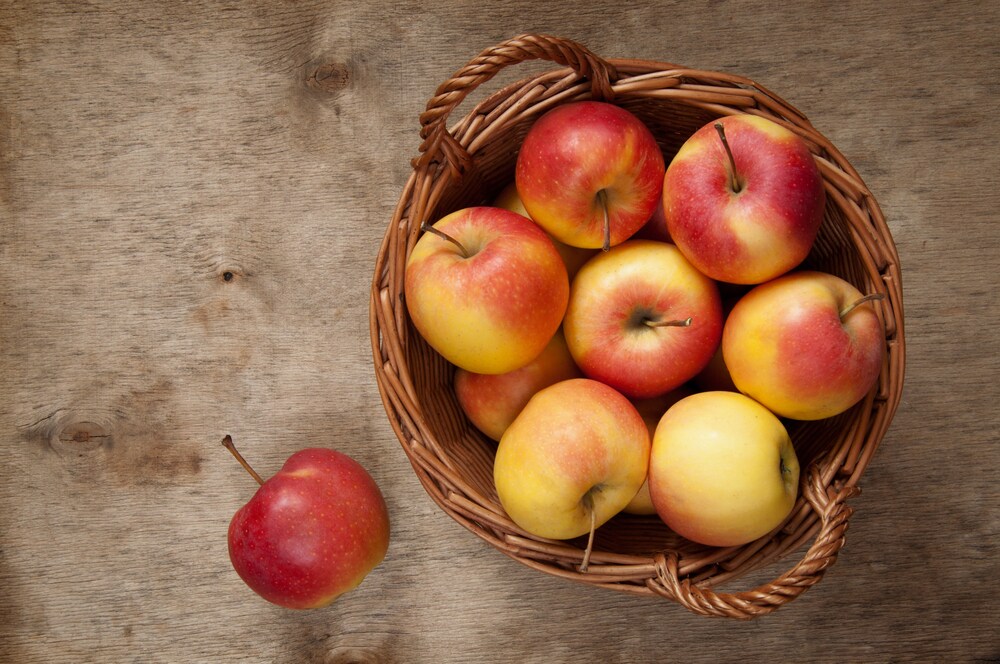 Red and yellow apples in a basket on a wooden table