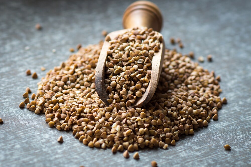 Buckwheat piled on a wooden spoon on a grey surface