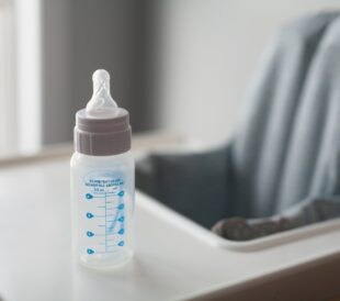 An empty baby bottle waits on a high chair, symbolizing the importance of food safety testing for Cronobacter in powdered infant formula