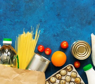 Food Home Delivery. Oil in a bottle, pasta, canned food, cereals, eggs, milk, fruits and vegetables on a blue rustic background. Donation and charity. Top view, flat lay,copy space.