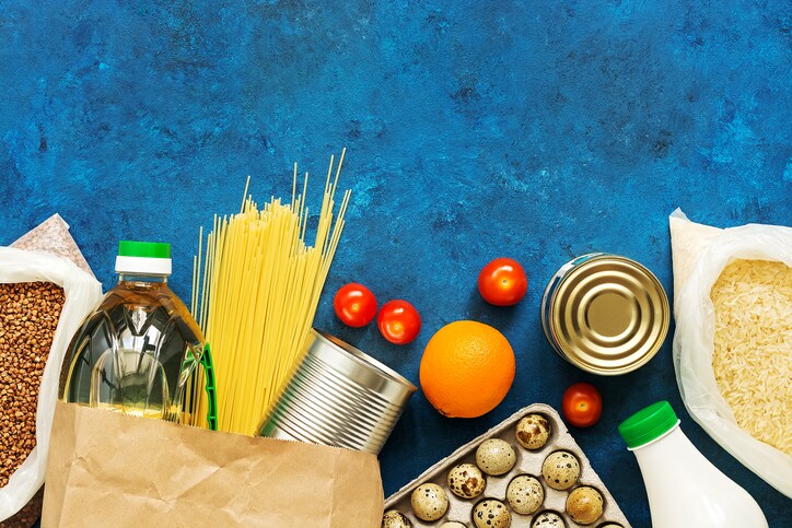 Food Home Delivery. Oil in a bottle, pasta, canned food, cereals, eggs, milk, fruits and vegetables on a blue rustic background. Donation and charity. Top view, flat lay,copy space.