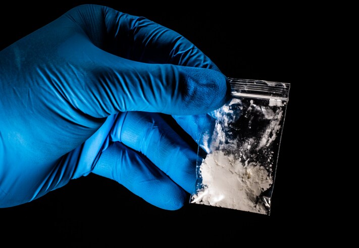 picture of gloved hand holding packed of white powder believed to be fentanyl