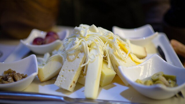 A beautiful cheese plate with several kinds of white cheese in the middle and small bowls of olives on the edges.